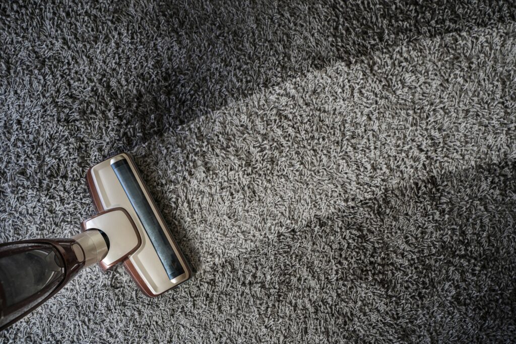 A vacuum cleaner glides over a grey carpet, leaving a clean path where the fibres appear lighter—a satisfying result of effective home cleaning.
