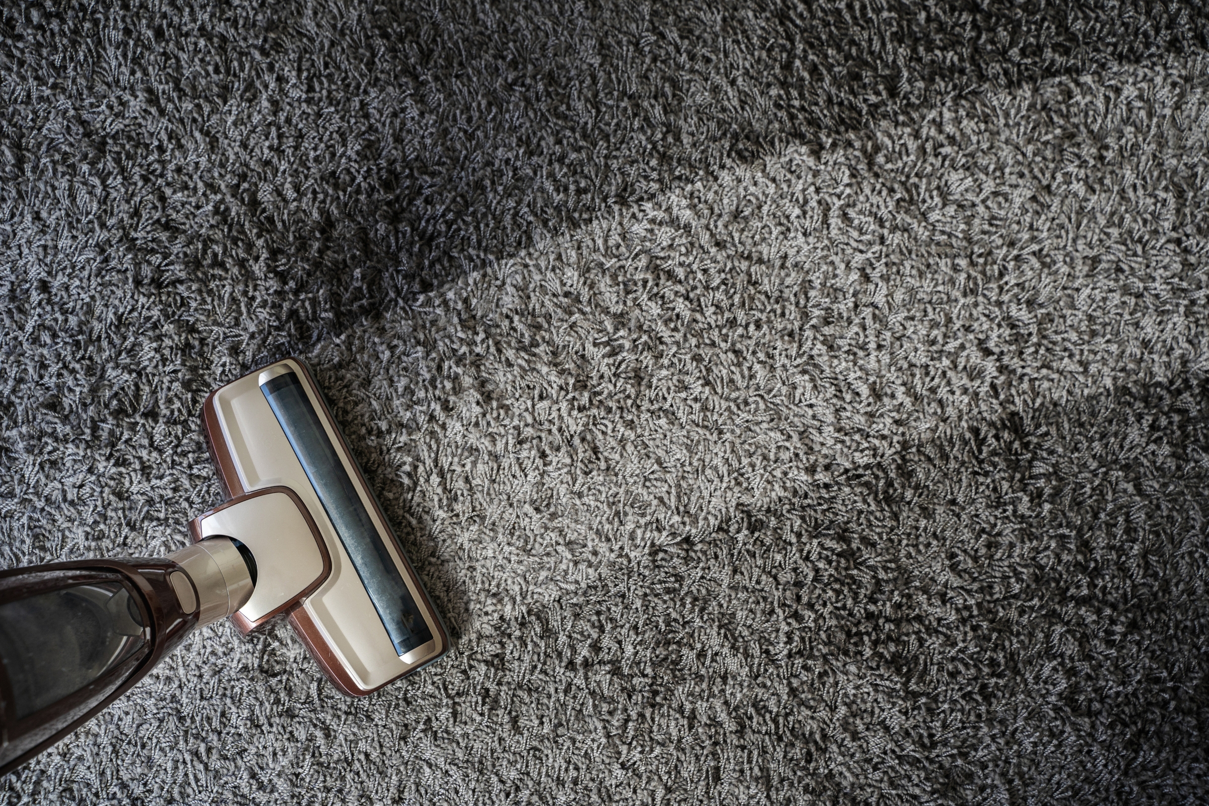 A vacuum cleaner glides over a grey carpet, leaving a clean path where the fibres appear lighter—a satisfying result of effective home cleaning.